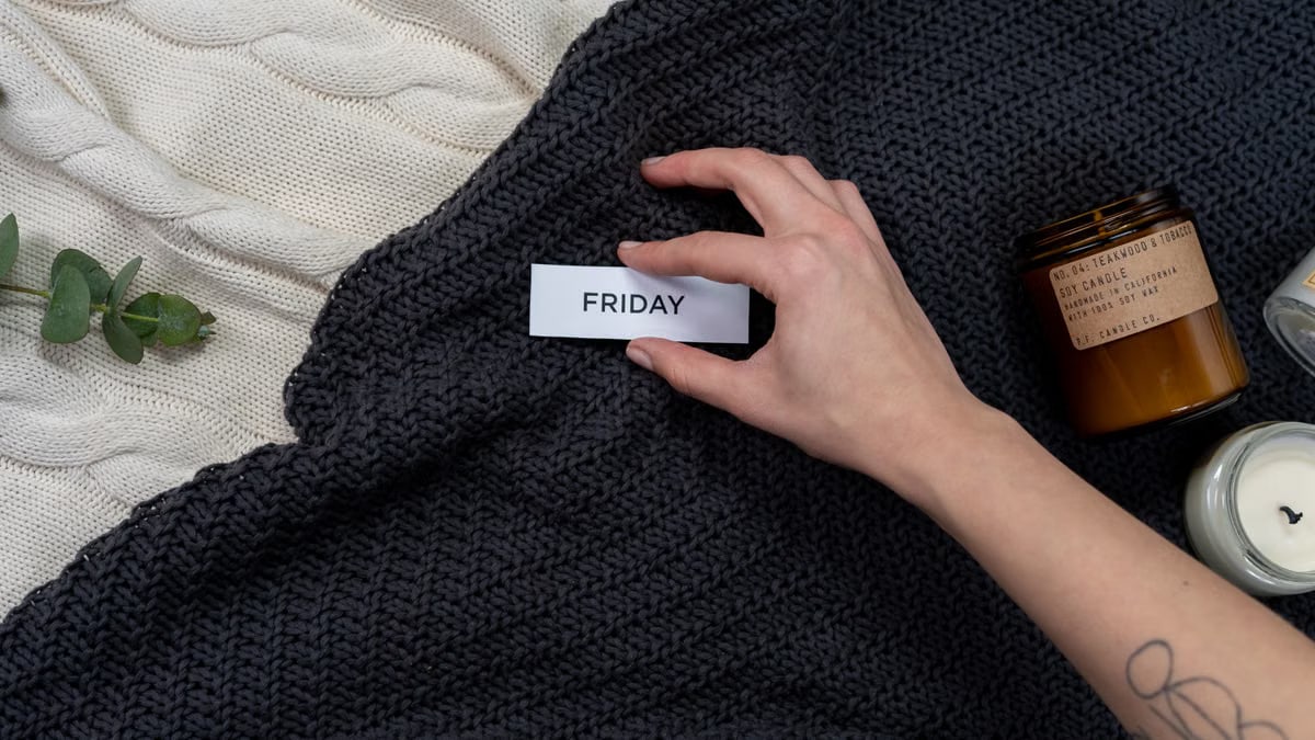 A warm, cozy flat lay featuring candles, a knitted blanket, and a 'Friday' tag, perfect for leisure or relaxation themes.