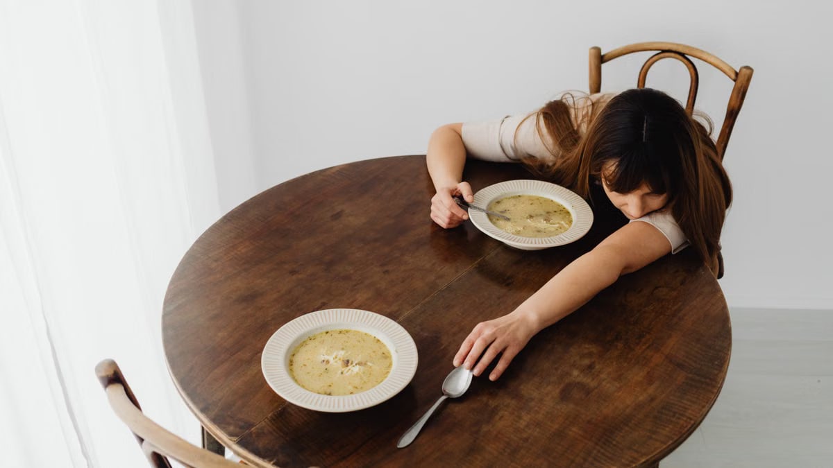 Woman lying down on a wooden table with two bowls of soup, creating a calm and serene scene.